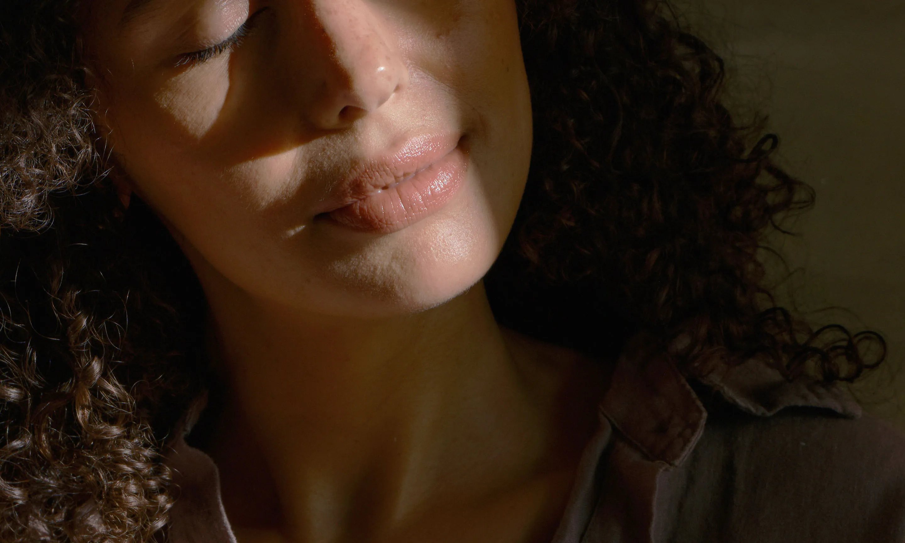 Close-up of a woman face in warm natural light, tilting her head back in a gentle neck stretch.