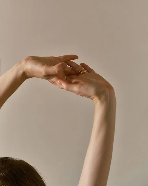 Person stretching their hands and wrists with arms raised.
