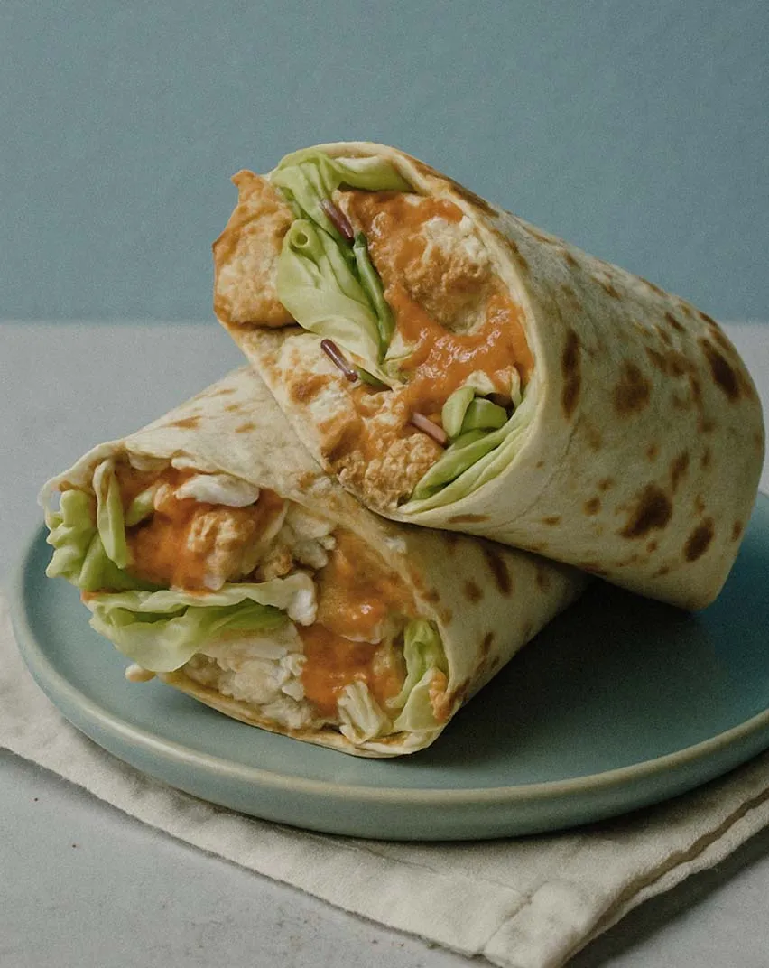 Tortilla wrap cut in half filled with chicken, lettuce, and sauce on a plate.